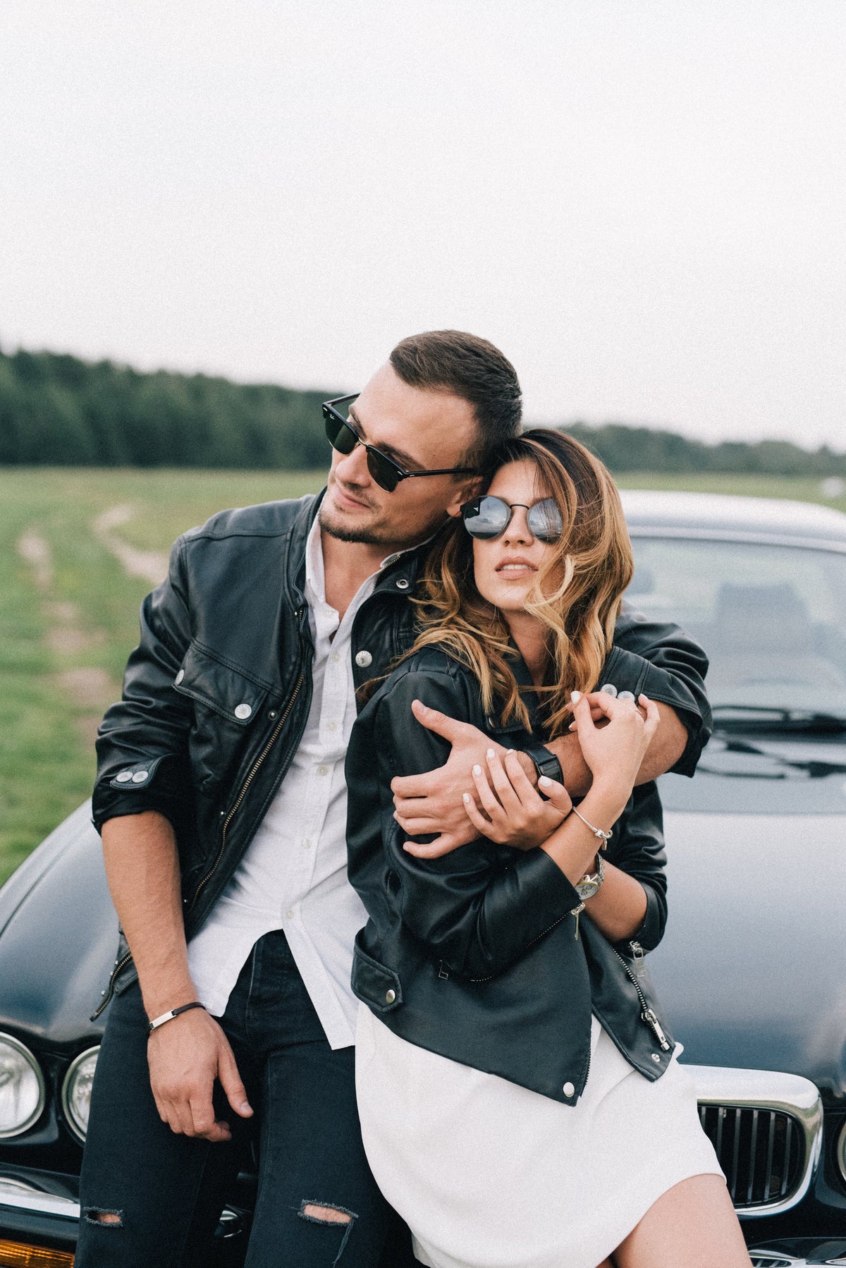 Couple on a date wearing leather jackets and leaning on a car bonnet
